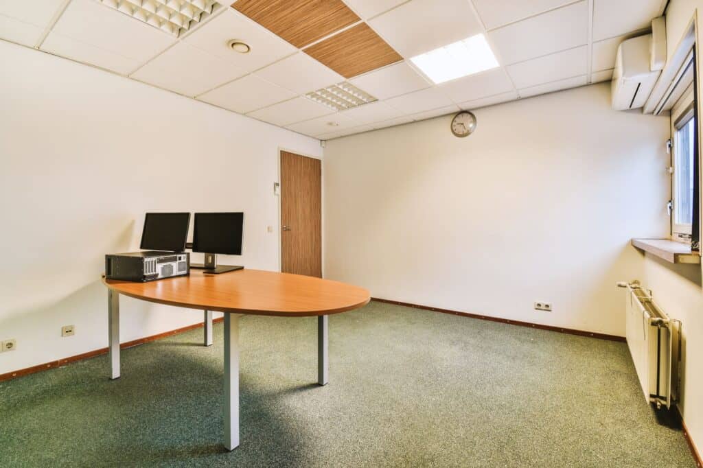A spacious room with two monitors and a processing unit on a big table.