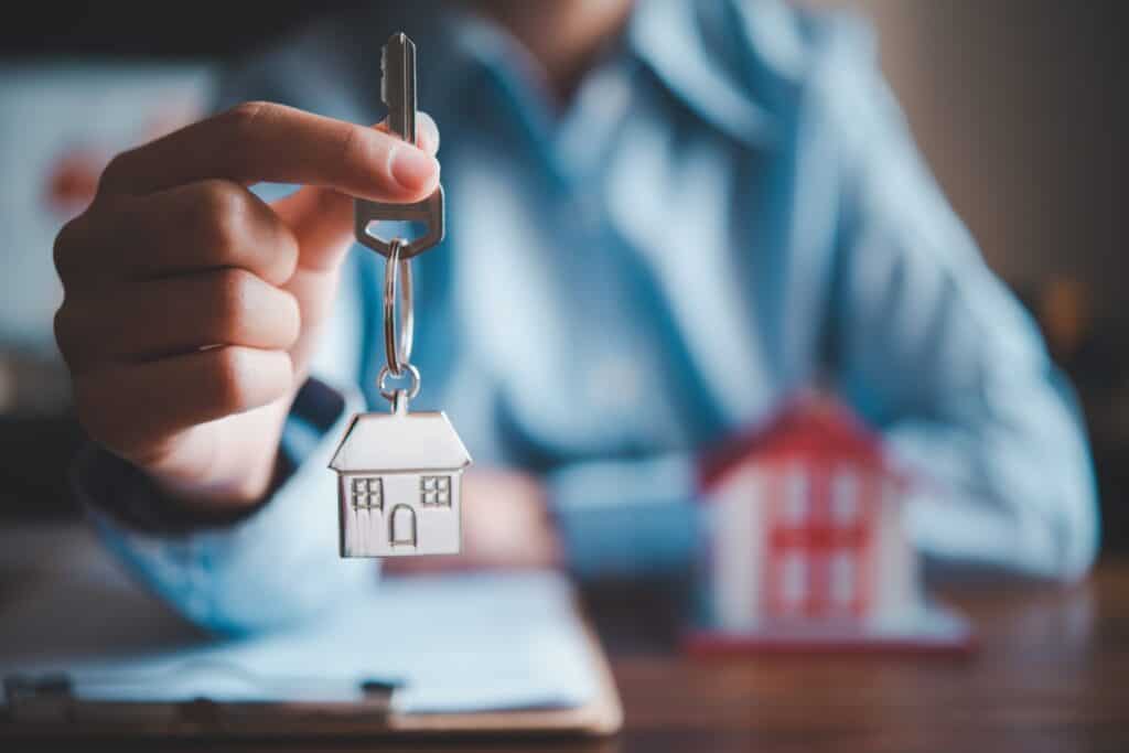 A salesperson is holding a house key and a house figurine in the background in the concept of housing options in Finchley.