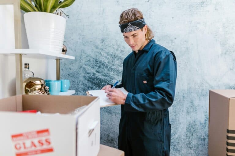A professional mover is holding a clipboard and pen and is surrounded by boxes in the concept of a Man and Van in Finchley.