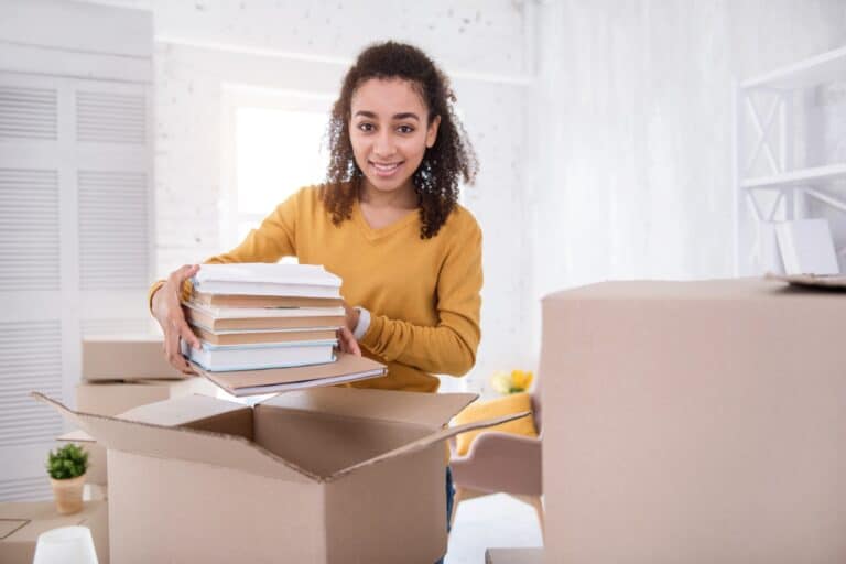 A student unpacking books from the carton after the relocation in the concept of 'How to Settle into a New Home After Moving'.