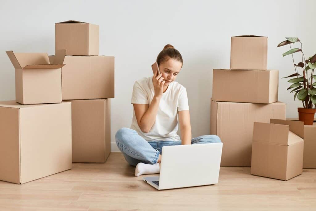 A woman is surrounded by boxes while on the phone with utility service in the concept of 'Changing Address and Updating Utilities After Moving to Finchley'.